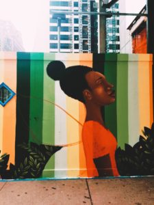 A painting on a wall with a Black girl with a red shirt closing her eyes