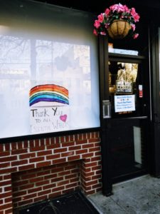 A red bricked storefront with a paper with a rainbow. Words read, "Thank you to all Healthcare workers" in a crayon