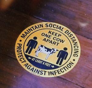 A yellow stickerreads, "Maintain Social Distancing - Protect Against Infection. Keep One Cow Apart - At Least 6 Feet."