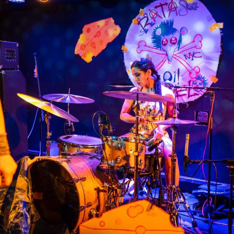 Drummer for Ratas En Zelo looking down. A giant decorative piece of cheese hangs above her